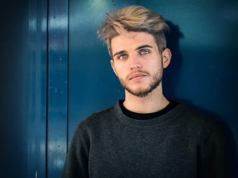 A man standing in front of a blue wall. Photo of a man posing in front of a vibrant blue wall, looking at camera