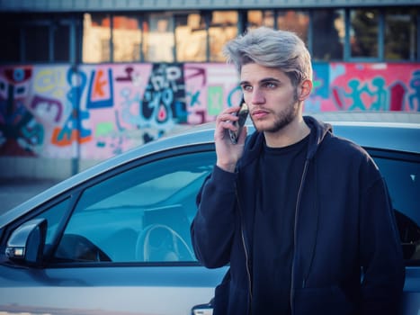 A man standing next to a car talking on a cell phone. Photo of a man talking on a cell phone next to a car