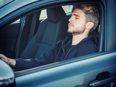 A man sitting in a car with his eyes closed, sleeping or falling asleep at the wheel