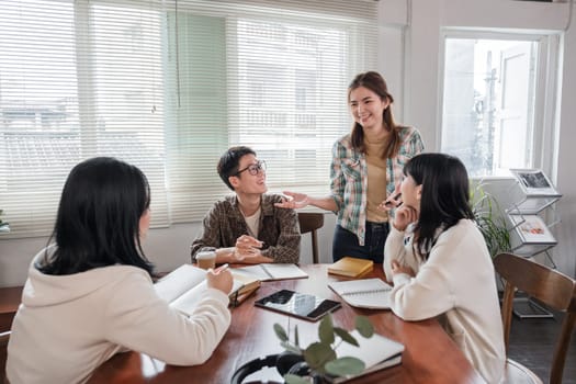 A cheerful and smart young Asian female is standing and sharing her ideas in a meeting with her team. University students, friendship, startups, teamwork.