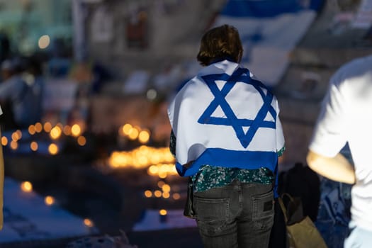 Lisbon, Portugal October 10, 2023. A woman at the memorial to the fallen Israelis in October 2023 at dusk, , with the flag of Israel on her shoulders. Mid. shot