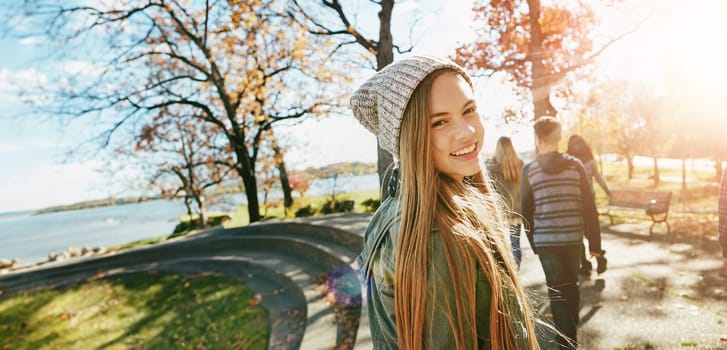 Teen girl in nature with friends, walk in park with autumn and sunshine, wellness with happiness in portrait. Youth outdoor, enjoy fresh air and bonding with smile, flare with adventure or travel.