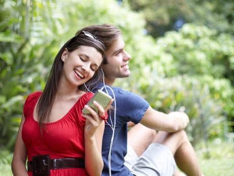 Happy, love and couple relax in a forest with music, conversation and bonding outdoor. Smile, romance and people in a park for date in nature while chilling on and having fun with weekend freedom.