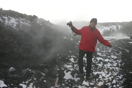 Man in red jacket with camera on the still steaming lava field of Mount Etna near Zafferano (Sicily)