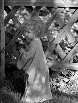 Small child with big t-shirt stands like a little angel in front of a hunter's fence