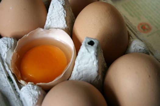 Brown eggs in an egg carton (one of them cracked)