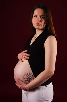 The photo shows a standing,pregnant woman with a tattoo