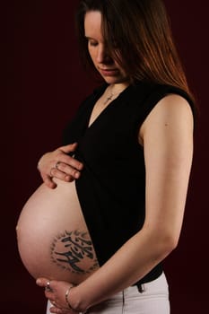 A pregnant woman stands,sensually looking at her stomach