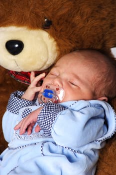 Photo shows a one-week-old baby leaning against a bear