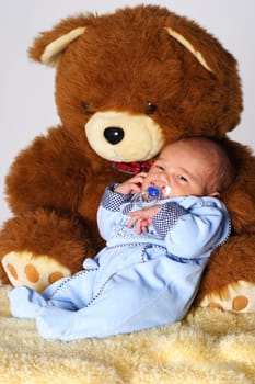 Photo shows a 1 week young baby with open eyes,leaning against a stuffed bear