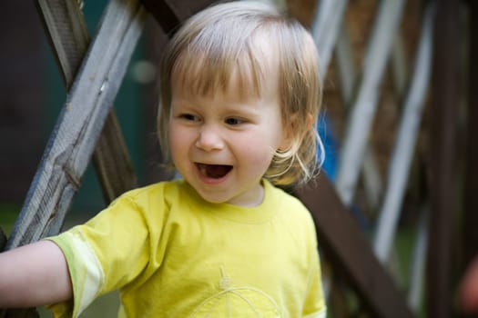 A little girl stands in front of a fence and has her mouth wide open..... As if she's calling someone or laughing out loud