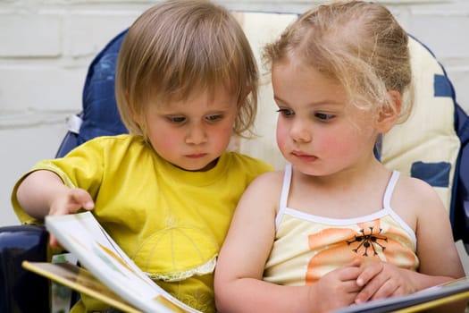 Two little friends sit on a chair and read a book together
