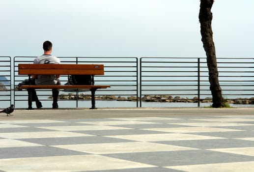Young man sitting on a bench on the beach.