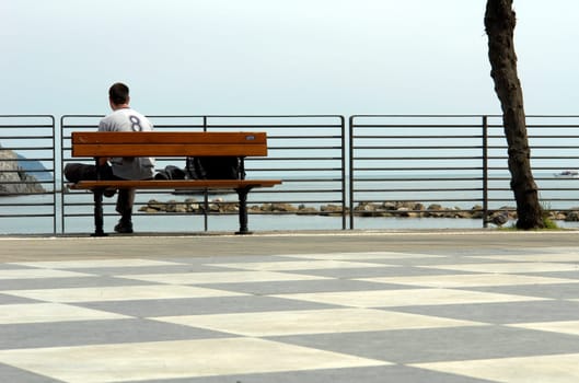 Young man sitting on a bench on the beach.