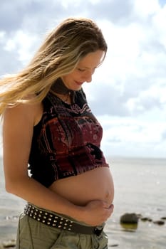 A young pregnant woman stands on the beach and feels the movements of the unborn child