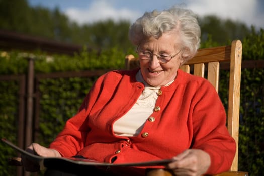 An elderly lady sits on a chair and reads a newspaper