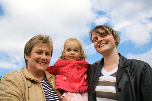 Mother,daughter and grandchild together in front of a blue,slightly cloudy sky