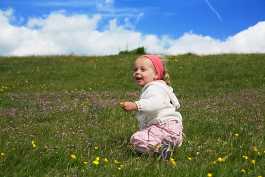A little girl plays on a summer meadow in front of a blue,slightly cloudy sky.
