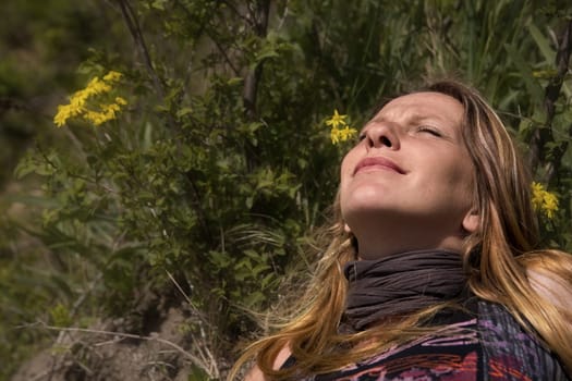 A young woman with her eyes closed while relaxing in the background yellow flowers