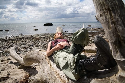 A young pregnant woman lies on a dead tree on the beach in the background the sea