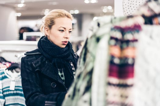 Woman shopping clothes. Shopper looking at clothing indoors in store. Beautiful blonde caucasian female model.