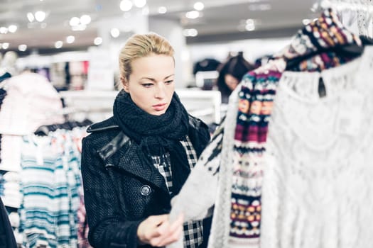 Woman shopping clothes. Shopper looking at clothing indoors in store. Beautiful blonde caucasian female model.