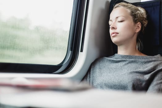 Blonde casual caucasian lady napping while traveling by train.