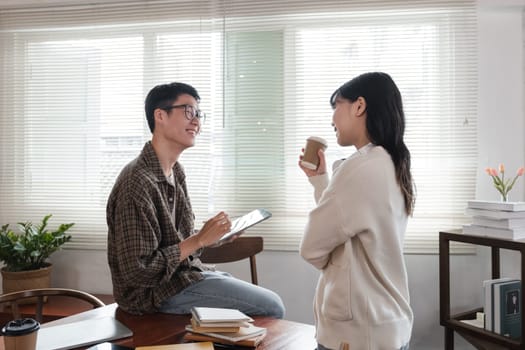 A happy young Asian man and a pretty girl are working on a laptop together, working on a co-project, sharing ideas and discussing work in a room..