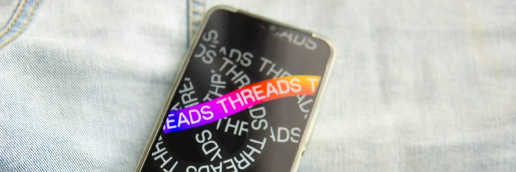 Tver, Russia - July 15, 2023, the threads logo on the smartphone screen lying on the jeans. The threads icon. The logo of the current application. Threads social network