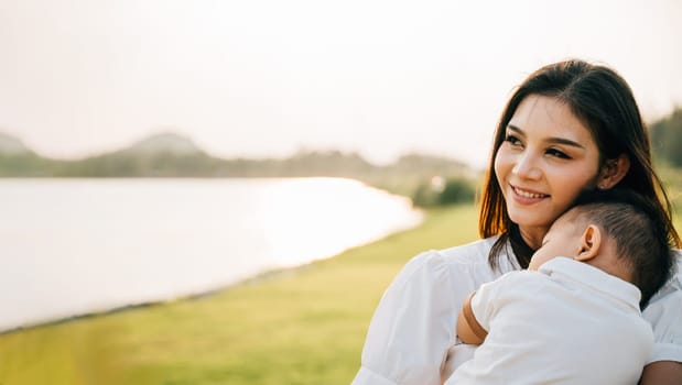 Family care. Happy beautiful mother holding baby sleeping son in the park at evening time before sunset, Portrait of mom hold newborn feeling happy and smiles in the garden nature outdoor, Mother Day