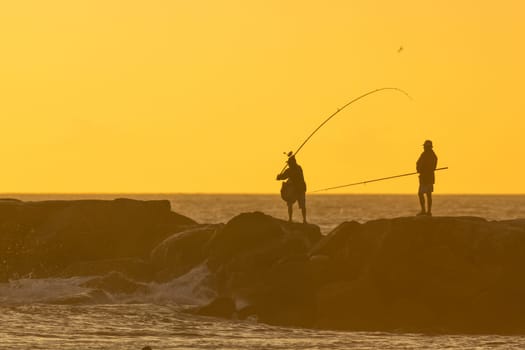 Fishermen are fishing standing on the rocks in the sea at sunset