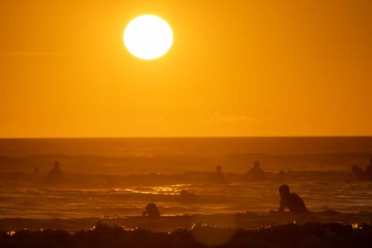 People swimming in the sea at bright orange sunset - huge shining sun. Mid shot