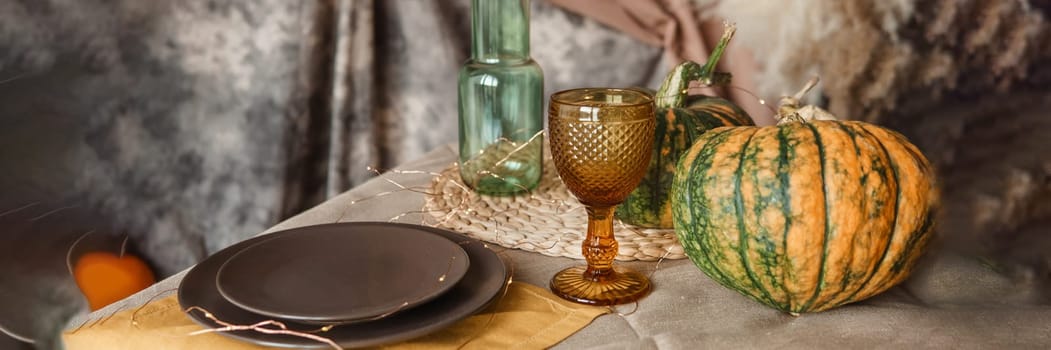 Autumn interior: a table covered with dishes, pumpkins, chair, casual arrangement of Japanese pampas grass. Interior in the photo Studio.