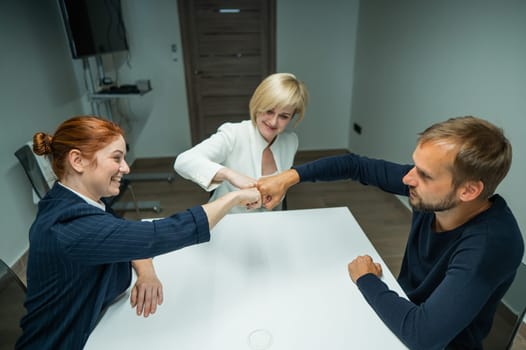Blond, red-haired woman and bearded man in suits in the office. Business people greet with fists in the conference room