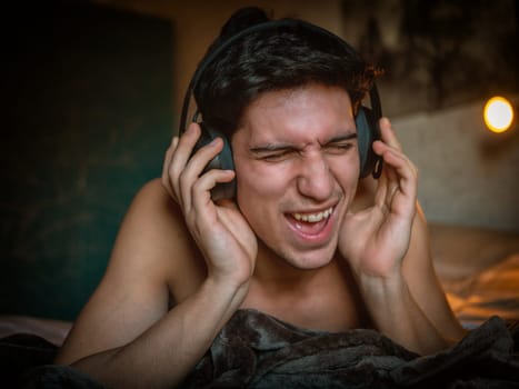 Attractive Young Man Using Headphones Lying Alone On His Bed, Listening to Music and Having a Good Time