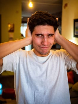 Too much noise: attractive young man covering his ears, indoor at home