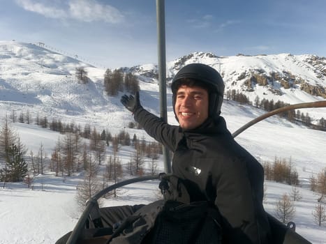 Portrait of handsome man in skiing suit sitting on chairlift rising up and looking at camera.