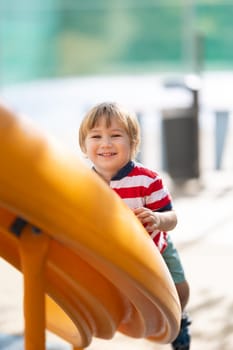 Cute smiling blonde boy climbing up the slide and looking in the camera. Vertical shot