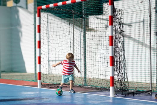 Little blonde smiling boy playing soccer - standing in the gates. Mid shot