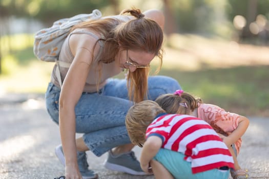 A woman sat down next to her two children in the park and looking down at the ground. Mid shot