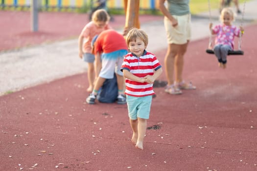 Little cute boy walking on the playground with other kids. Mid shot