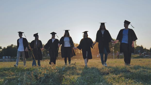 College graduates walk at sunset holding hands