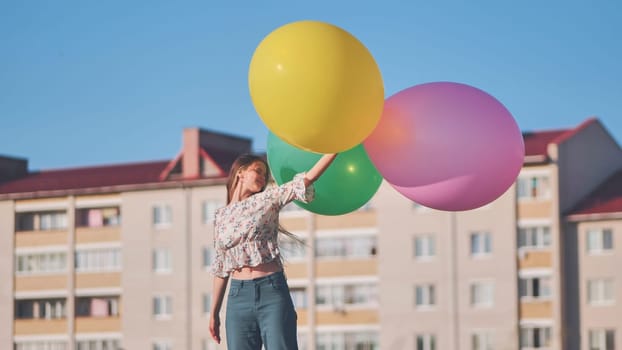 A girl happily poses with large with colorful balloons in the city