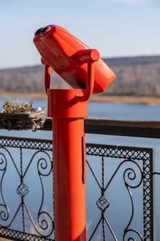 Public stationary binoculars on the banks of the river in summer or autumn to look at nature, coin-operated red metal binoculars.