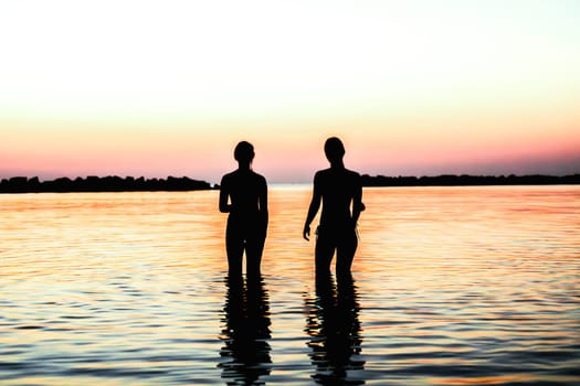 two figures walk on the sea at dawn.