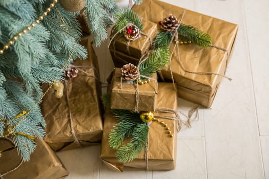 Many boxes of Christmas gifts in eco-friendly craft paper packaging and twine on the floor under a green Christmas tree