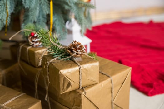 Many boxes of Christmas gifts in eco-friendly craft paper packaging and twine on the floor under a green Christmas tree