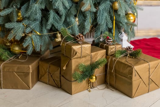 Many boxes of Christmas gifts in eco-friendly craft paper packaging and twine on the floor under a green Christmas tree