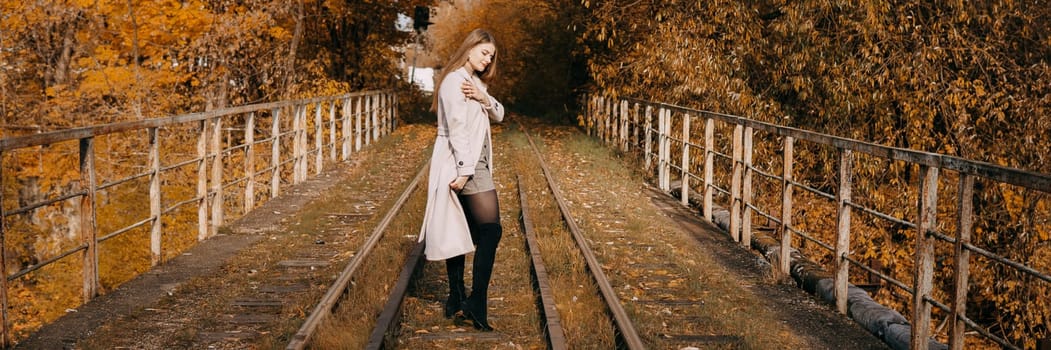 A beautiful long-haired woman walks through the autumn streets. Railway, autumn leaves, a woman in a light coat.