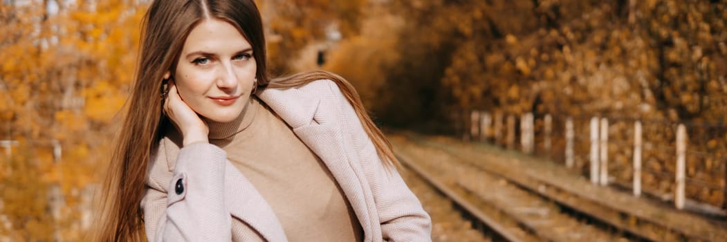 A beautiful long-haired woman walks through the autumn streets. Railway, autumn leaves, a woman in a light coat.